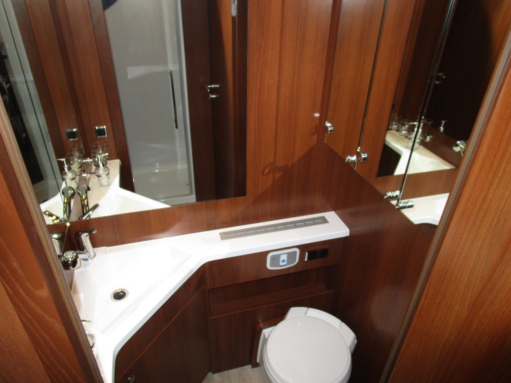 Modsat brusekabinen er toilettet. Det er et drejetoilet med god plads omkring. Rummet er med store spejle, en integreret håndvask og god plads omkring vasken. Der er godt med skabsplads og spejle på skabsdørene.